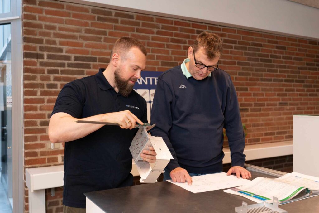 To mænd gennemgår en metal prototype og tegninger på et værksted.